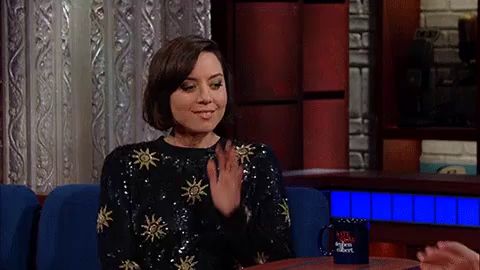 a woman in a sequined sweater is waving her hand while sitting in a couch .