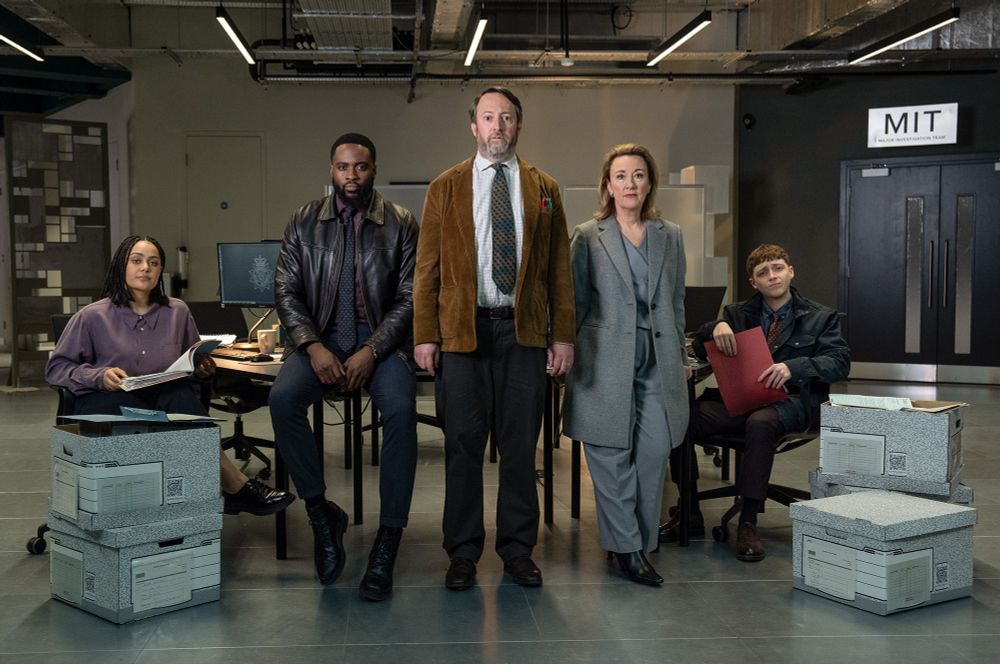 Group shot of Izuka Hoyle, Dipo Ola, David Mitchell (in the centre), Dorothy Atkinson and Gerran Howell in a modern police building surrounded by boxes of files