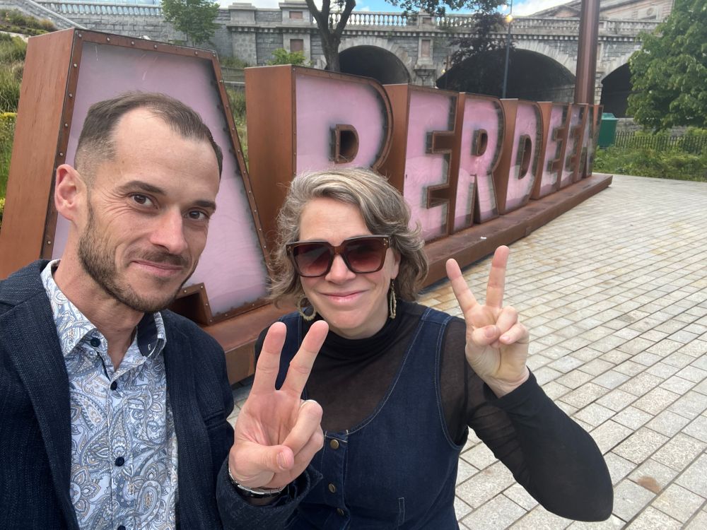 Jonathan Burgess and Anna Brown pose in front of a large pink Aberdeen sign.