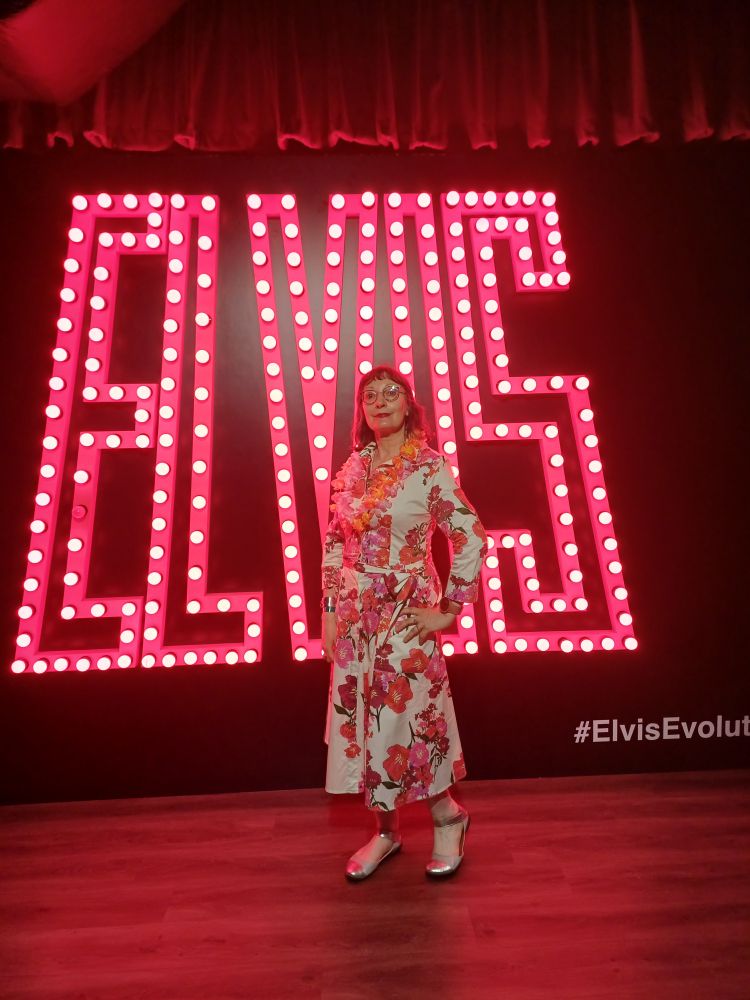 Me in a flowery dress standing in front of the word Elvis written in pink lights.