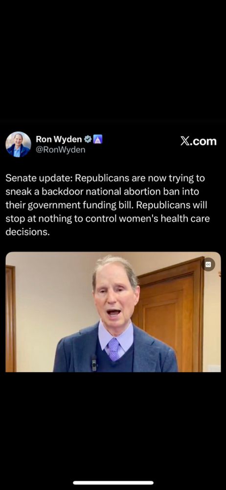 Man with blue suit jacket standing in front of wood door 