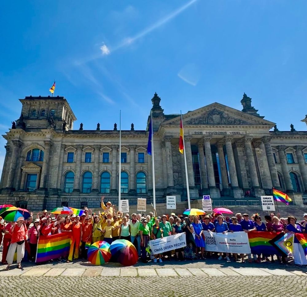 Große Gruppe Omas gegen Rechts, in Regenbogenfarben gekleidet, vor dem Reichstagsgebäude, mit Bannern, Schildern, Schirmen, bei strahlend blauem Himmel 