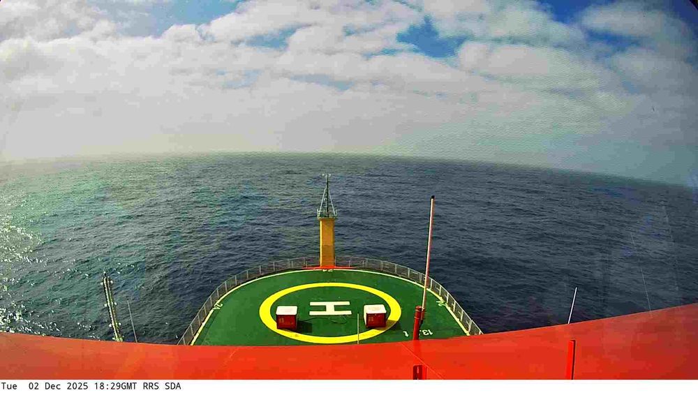 View from a webcam mounted on the RRS Sir David Attenborough boat. Typically you'd see the front of the ship with a helipad, and the sea waters surrounding the ship. Depending on the current location of the ship, the scenery may include icebergs and industrial ports.