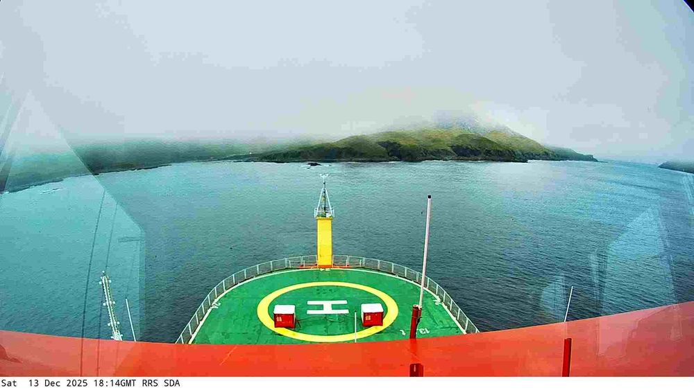 View from a webcam mounted on the RRS Sir David Attenborough boat. Typically you'd see the front of the ship with a helipad, and the sea waters surrounding the ship. Depending on the current location of the ship, the scenery may include icebergs and industrial ports.