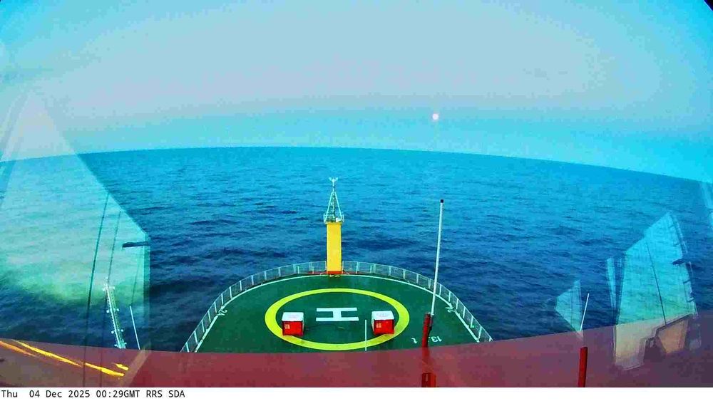 View from a webcam mounted on the RRS Sir David Attenborough boat. Typically you'd see the front of the ship with a helipad, and the sea waters surrounding the ship. Depending on the current location of the ship, the scenery may include icebergs and industrial ports.