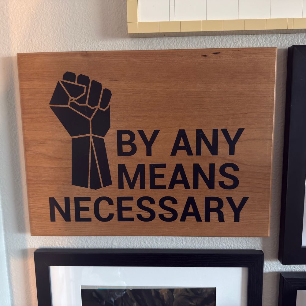 black ‘by any means necessary’ text next to a clenched fist on wooden background 
