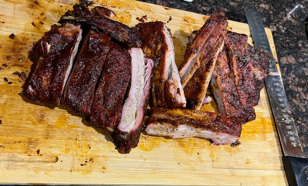 Rack of ribs, sliced and lined in a row on a light brown cutting board, with a long slicing knife lying next to it.