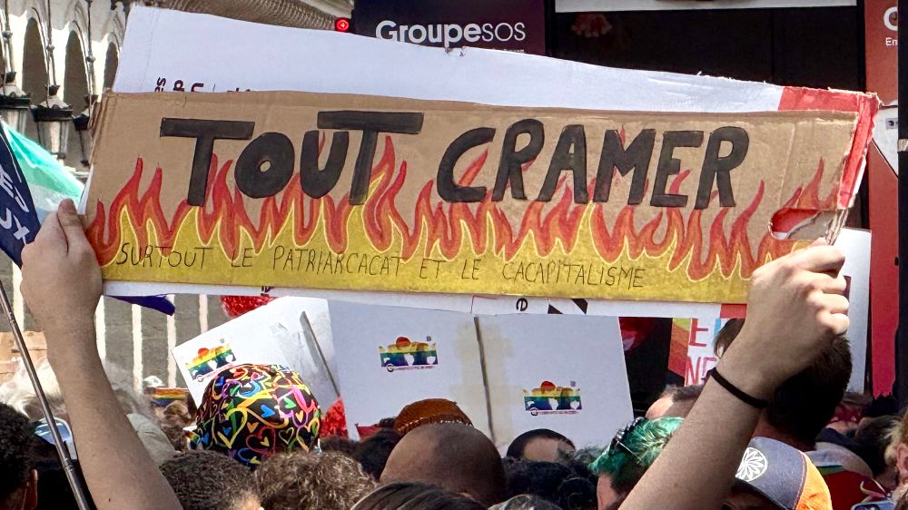Panneau aperçu lors de la pride parisienne. Il écrit : TOUT CRAMER (avec des flammes dessinées sur toute la largeur du panneau)