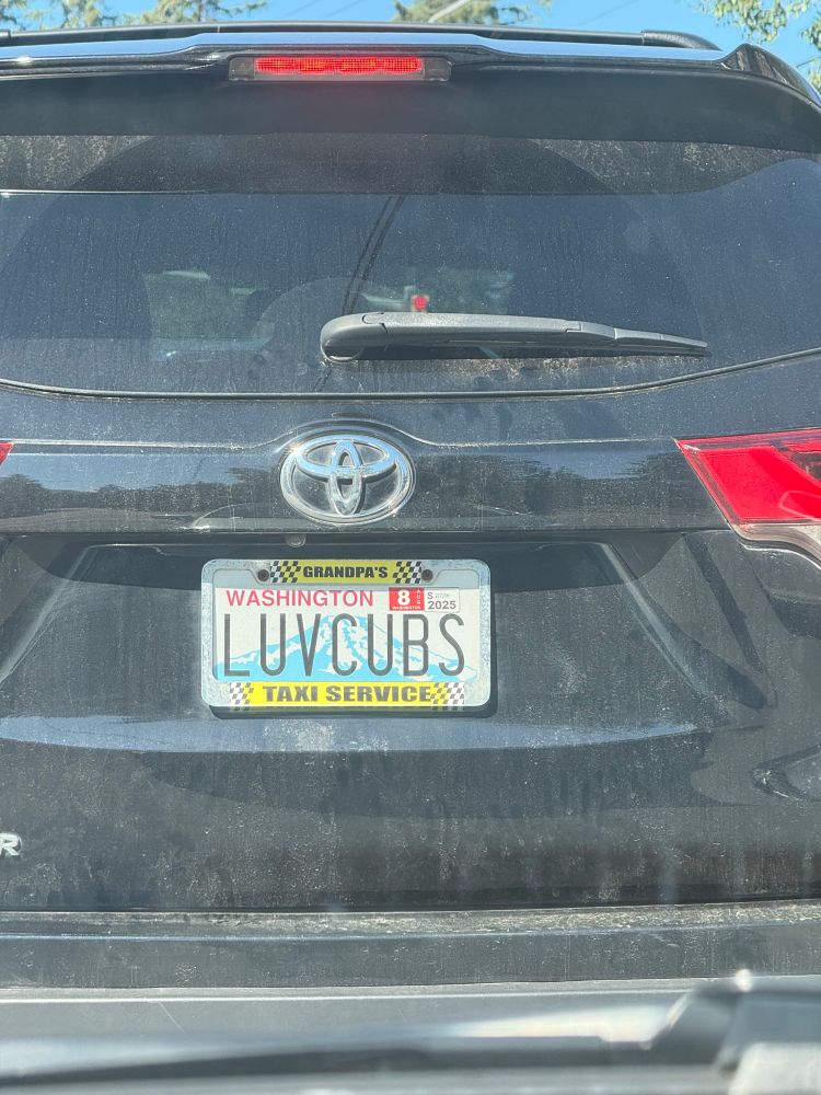 Photo of a Washington license plate on a black SUV that says “LUVCUBS” With a frame that says “grandpa’s taxi service”