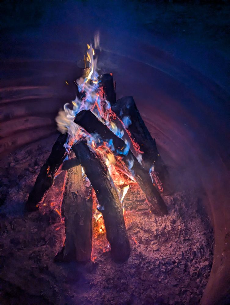 A smoldering campfire inside a drum where the flames are blue 