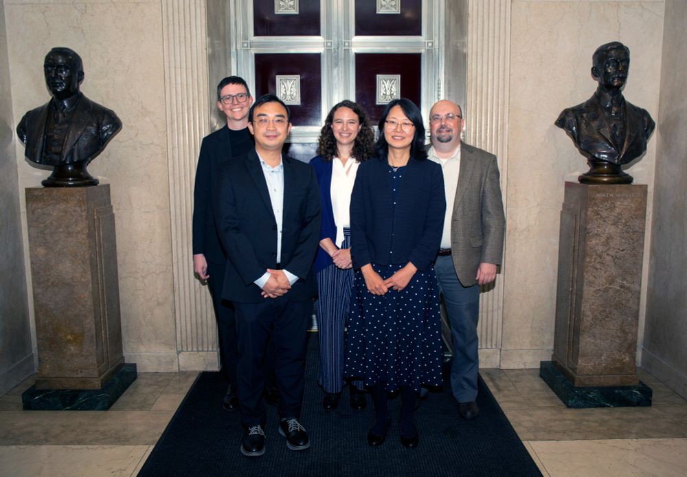 Five faculty members stand in between two busts.