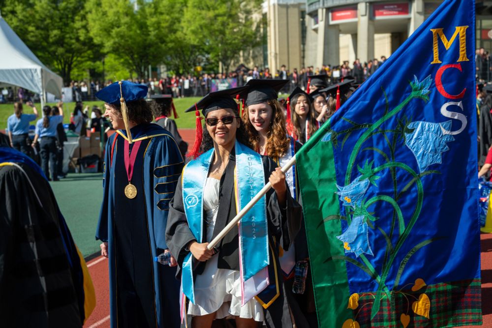 A student carries the flag of the Mellon College of Science while leading other students in a procession.