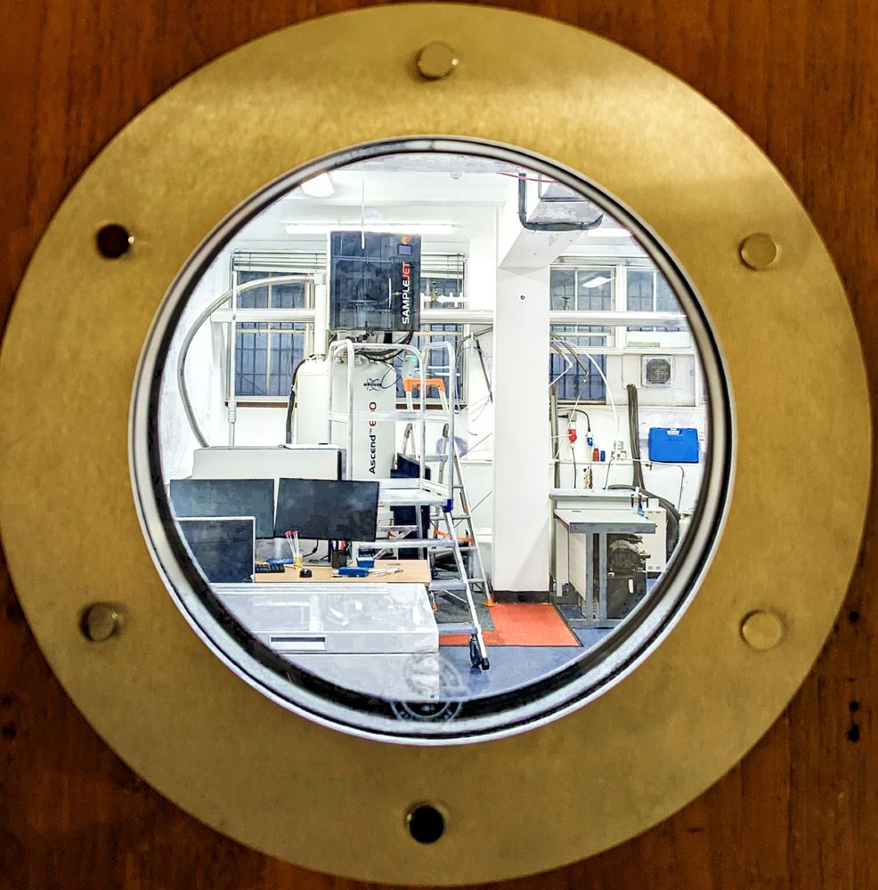 View of the UCL School of Pharmacy's 600 MHz spectrometer through a bronze-rimmed porthole in a wooden door