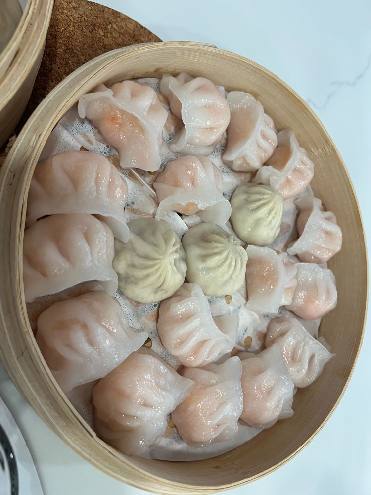 A steamer basket filled with ha gow (shrimp crescent dumplings) and three XLB pork soup dumplings 