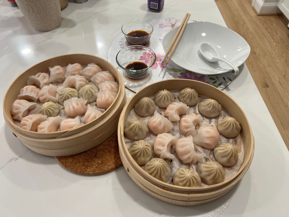 Two full steamer baskets of dumplings with dipping sauces and a soup spoon and chopsticks