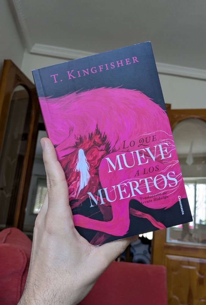 Foto de una mano sujetando el libro, en cuya cubierta se observa a una figura blanca internándose en Las vísceras de una liebre gigante y rosa. 
