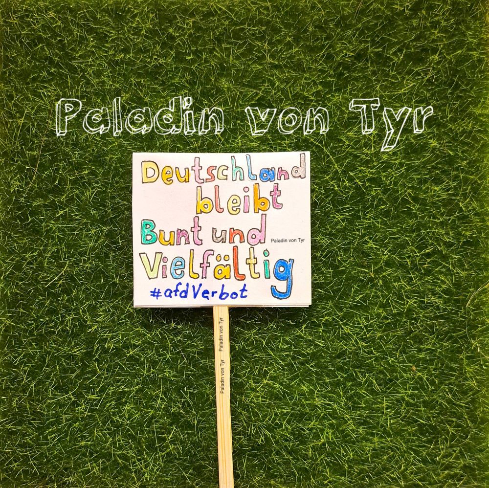 Auf einer grünen Wiese (kleines Stück Kunstgras aus der Bastelecke) liegt ein Schild.
Auf den Schild steht: "Deutschland bleibt Bunt und Vielfältig # a f d Verbot