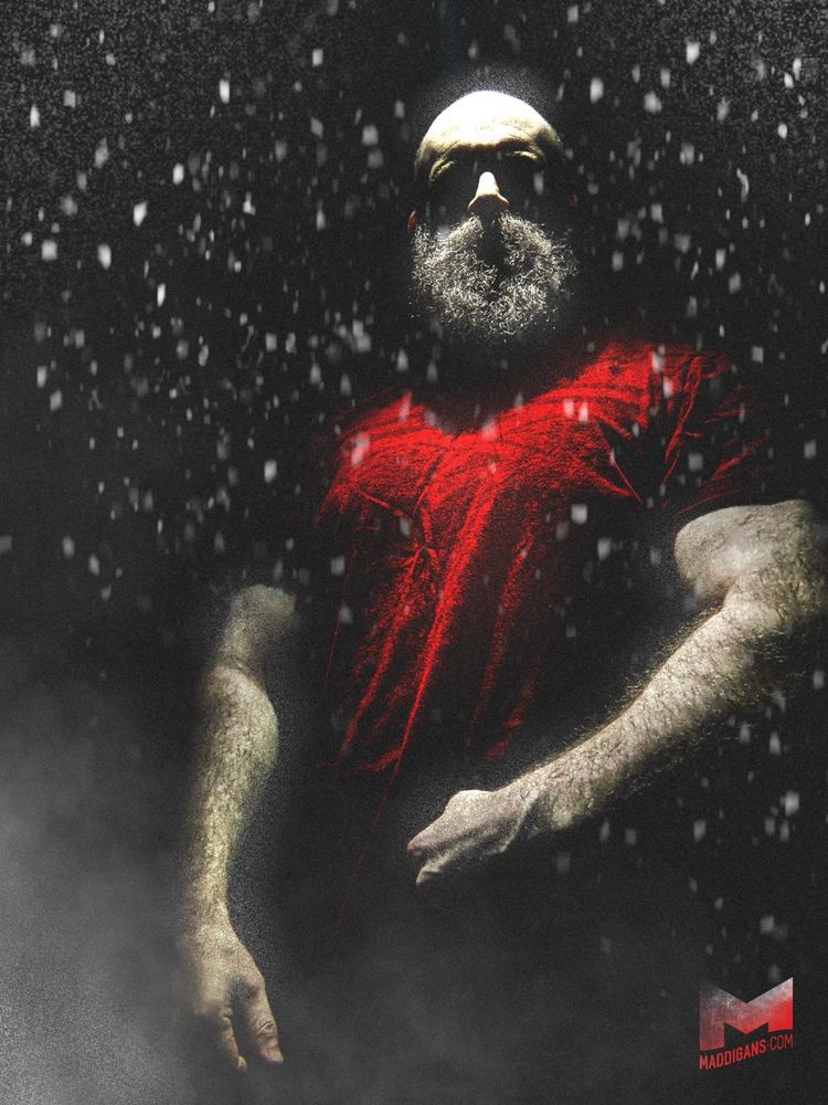 Mads standing in the shadows looking like Santa in a red shirt with light beaming down from above.