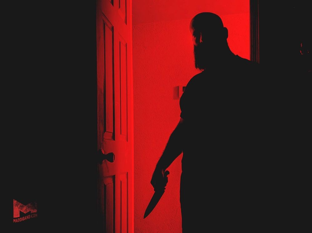 Silhouette of Mads standing in the doorway with a knife and red light casting over. 