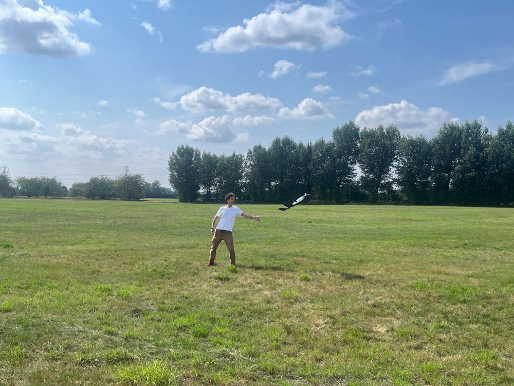 A photo of a man launching the ebee UAV in a grassy field. There are trees in the distance and white fluffy clouds in a blue sky.
