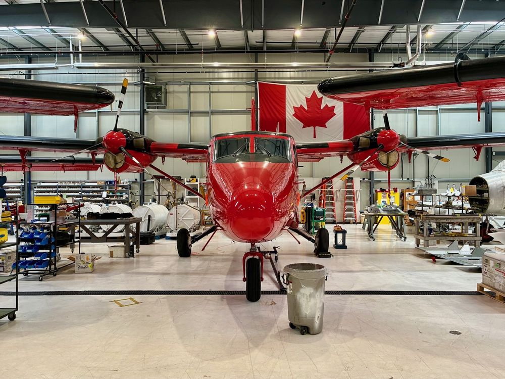A photo of BAS's red Twin Otter plane in a hangar/workshop. A Canadian flag can be seen in the background.