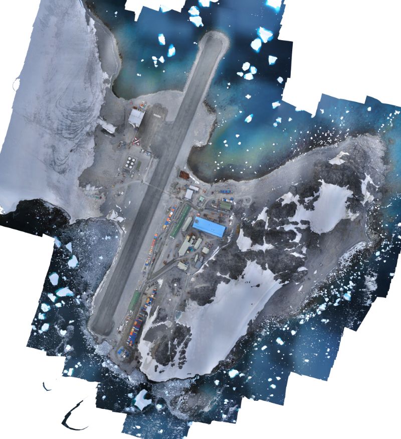 An image of Rothera Research Station, Rothera Point, on Adelaide Island. There is a bright blue building in the centre of the image which is the new Discovery Building. You can also see patches of snow on the point, and there are small icebergs floating in the surrounding water.