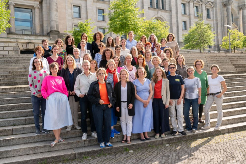 48 Geschäftsführer*innen stehen in lockeren Reihen auf einer Treppe im Freien, im Hintergrund ist der Reichstag zu sehen. Das Bild ist dem Foto des sogenannten Investitionsgipfels im Bundeskanzleramt nachempfunden, das aufgrund seiner männerdominierten Einseitigkeit vor Kurzem viel Wellen geschlagen hat.