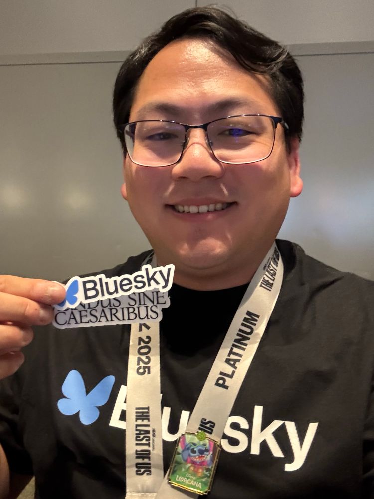 Daniel wearing a Bluesky tshirt and a SXSW lanyard holding up stickers