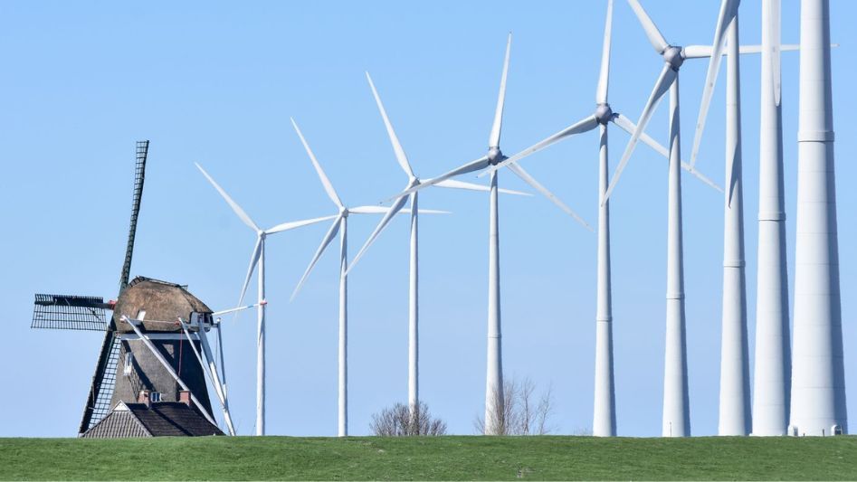 Photo: a row of modern, sleek wind turbines next to a clunky traditional windmill.