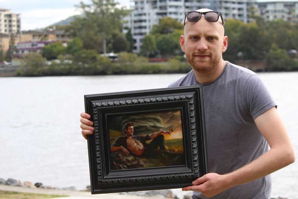 A man holds the framed photo by the Brisbane Riverside.
