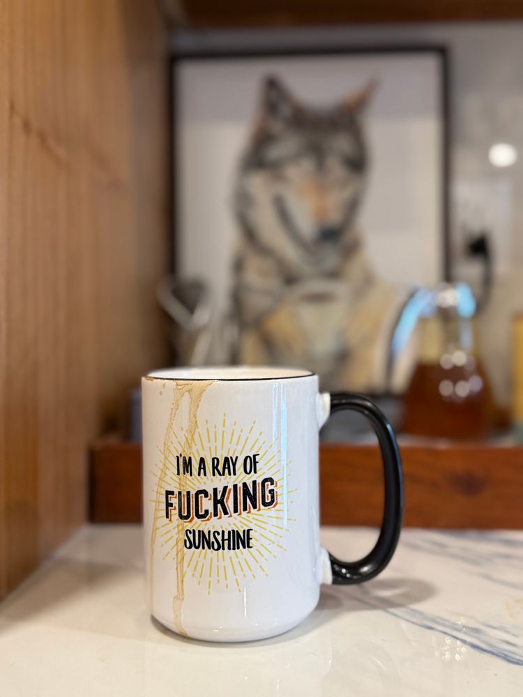 Overflowing coffee cup with the words I’m a Ray of Fucking Sunshine printed on cup