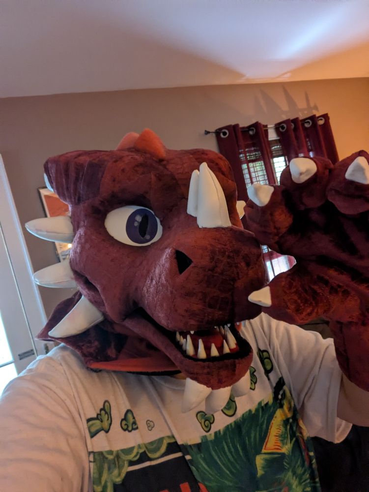 A red dragon fursuiter waving at the camera taking a selfie 