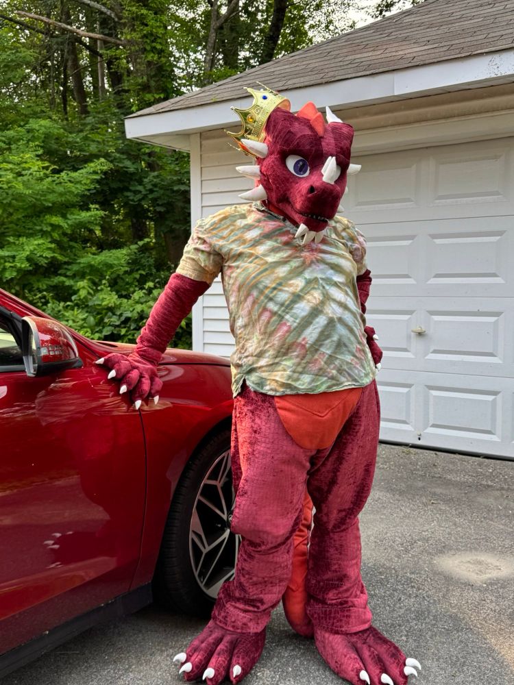 A red dragon fursuiter wearing a shirt leaning on a red car