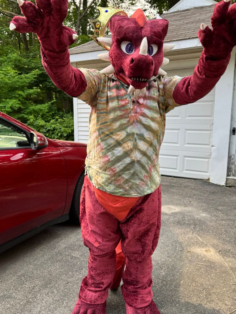 A red dragon fursuiter wearing a shirt opening his claws at the viewer, in a more silly way instead of threatening 