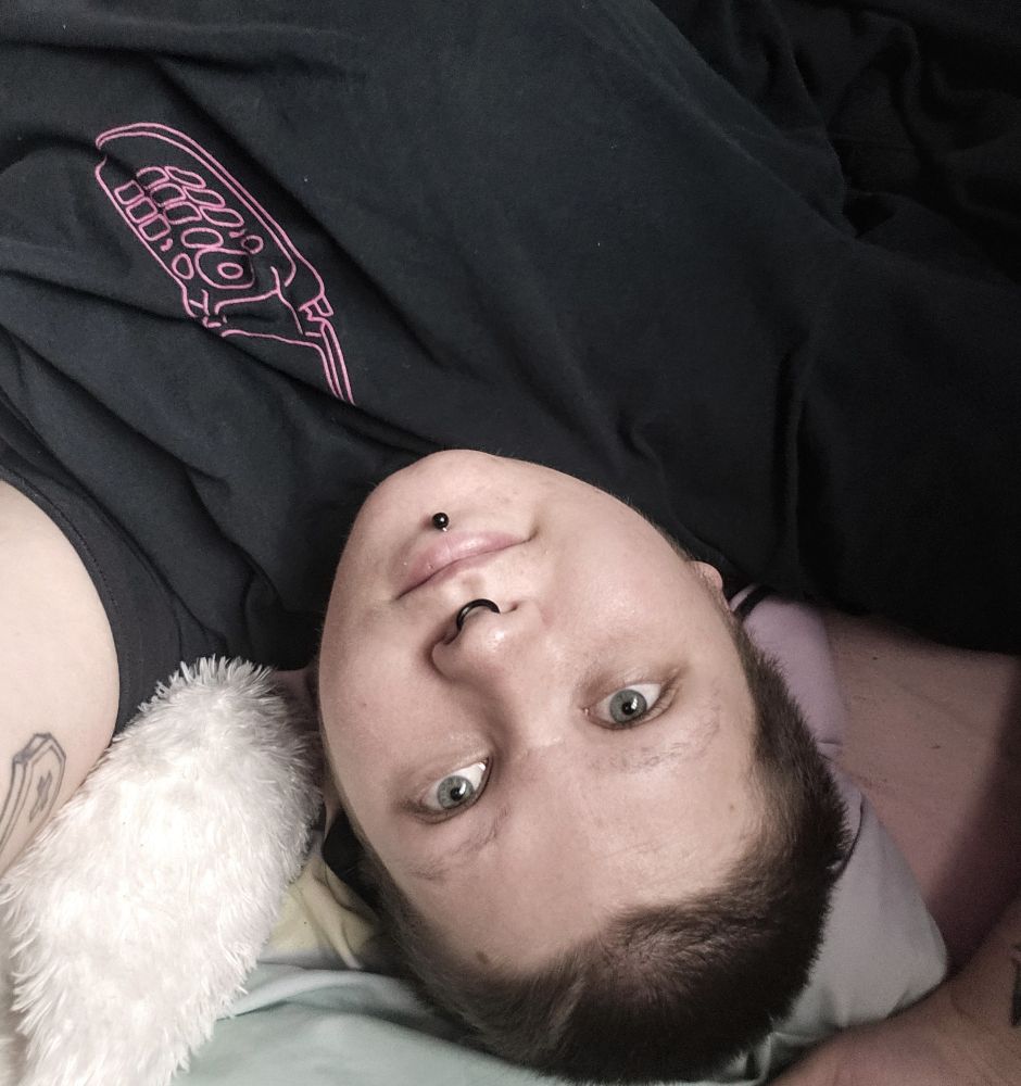 Upside down selfie of Bat in a black t-shirt, lying on its bed & smiling at the camera.