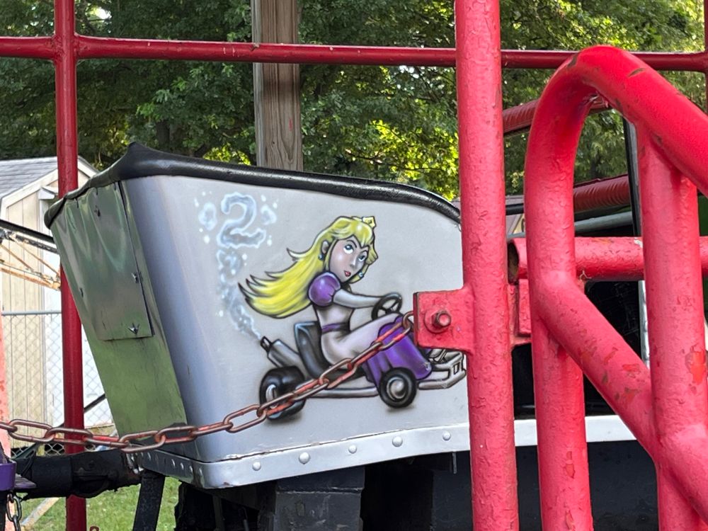 A silver roller coaster cart with a very bad Princess Peach painted on the side