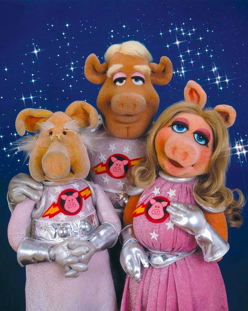 Pigs In Space! Dr. Strangepork (an old Muppet pig with bushy eyebrows), Link Hogthrob (a young handsome Muppet pig with blond hair), and Miss Piggy (a young beautiful Muppet pig with long blond hair) wear pink spacesuits.