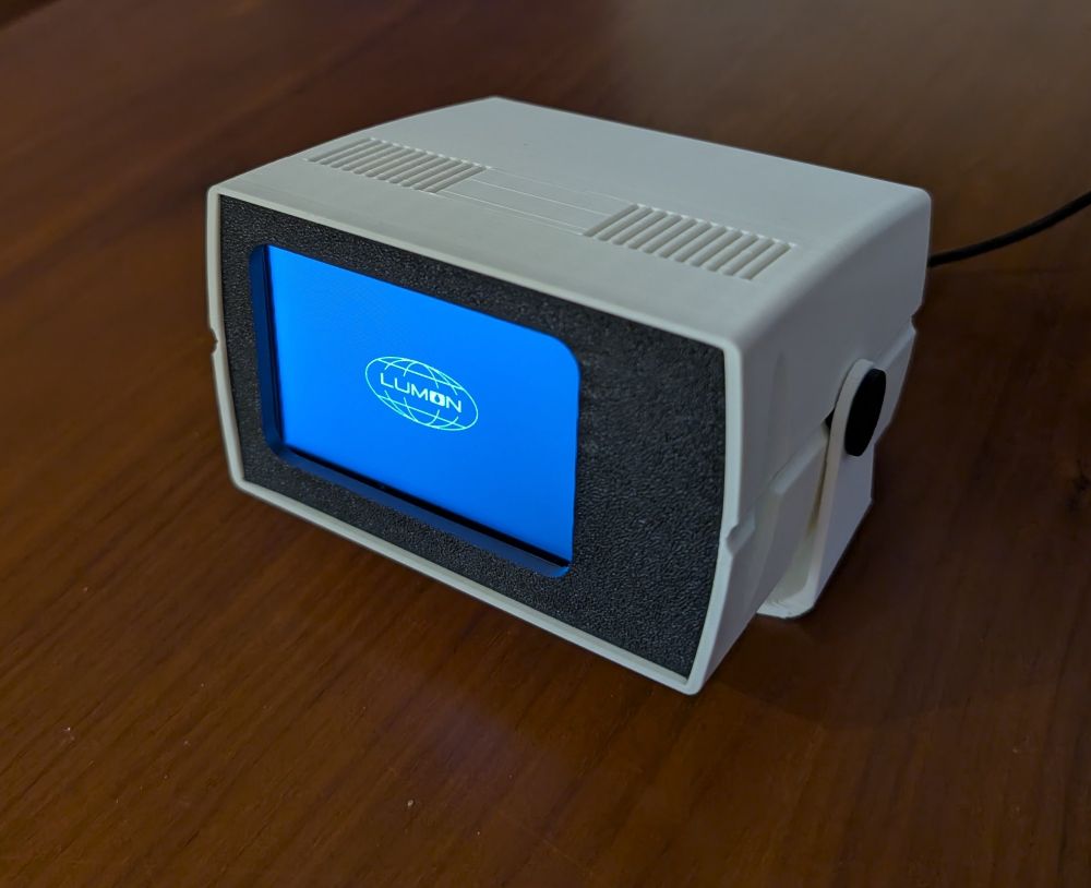 An exceptionally tiny (3.5" screen) Macrodata Refinement Terminal from the TV show Severance, powered on with a black and white "LUMON" logo 