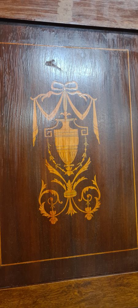 dark wood with a lighter warm toned inlay of a greco/roman style pot, floral motifs underneath, and ribbon swag on top.