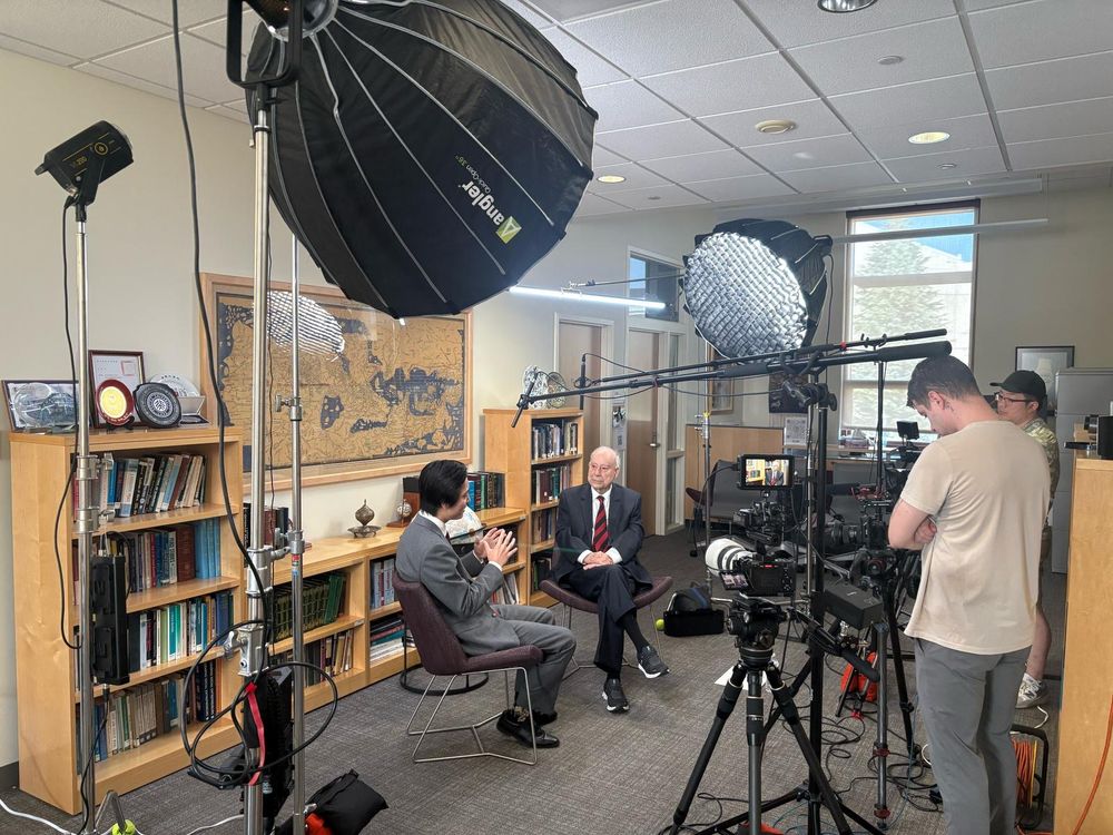 Behind-the-scenes picture of podcast filming. Two people surrounded by camera equipment.