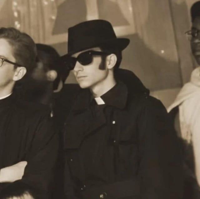 Rumor has it that this is a picture of Pope Leo as a very young man back in 1982. He's a wearing a fedora, wayfarer sunglasses, a black trenchcoat and his priest collar is visible. He's on a literal mission from God.