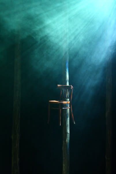 A chair hanging from a tree trunk with light shining behind it