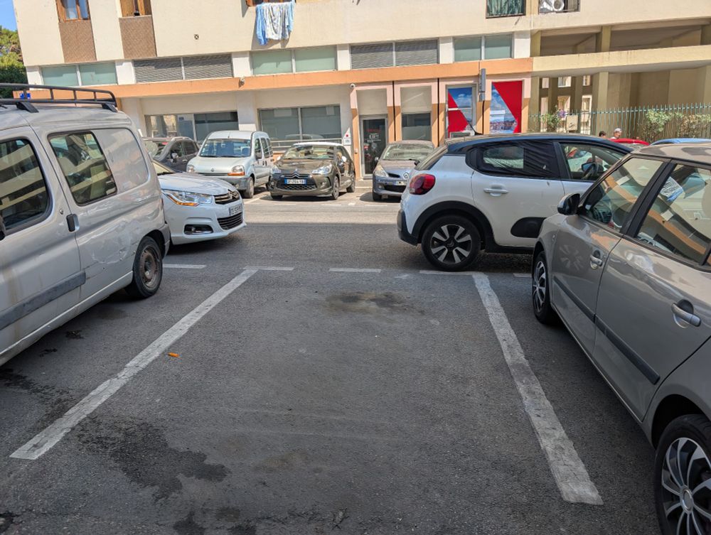 Une place de stationnement vide avec 2 voitures garée en part et d'autre de cette place, sur la route