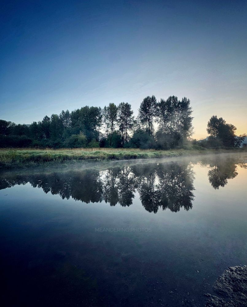 A mimicked tree line reflects in the water with a soft dusting of mist dancing along the vista. 