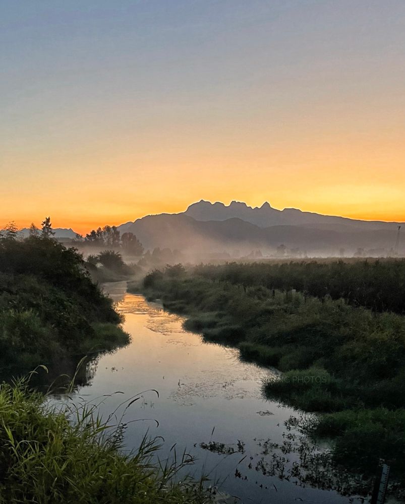 Hues of tangerine and yellow paint the mountains backdrop as mist rises from the waterway below. 