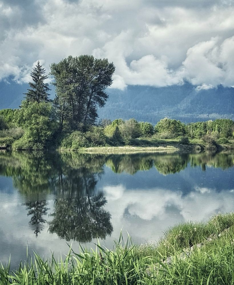 A multitude of green shades trim the lining of the waterway reflecting as the low clouds hide the mountains. 