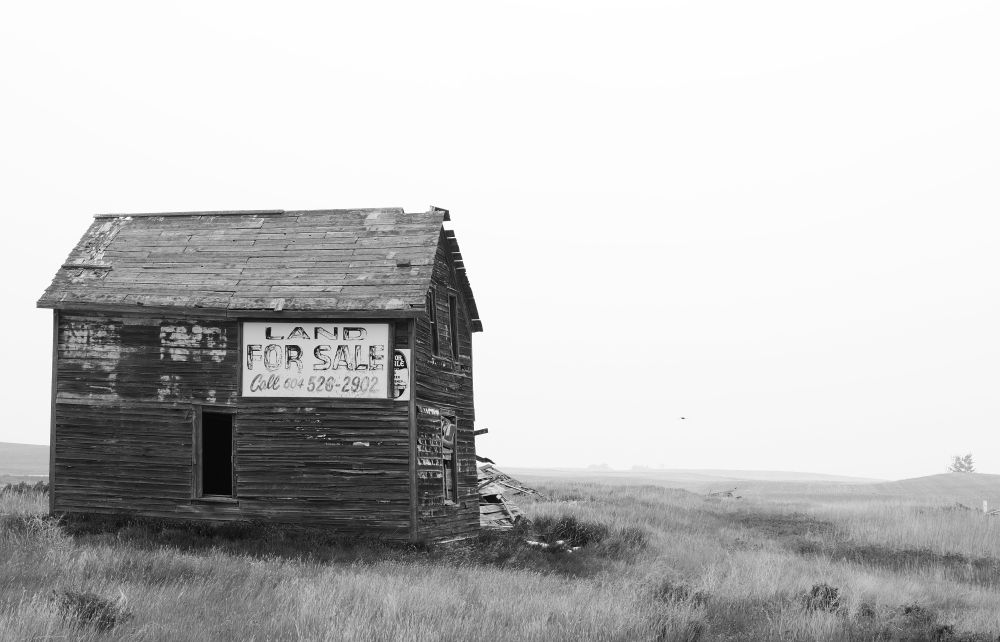 Black and white photo of an old building with the sign Land for Sale