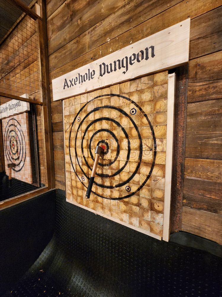 Image of an axe throwing target board down range. There is a hand axe buried in the center just south of middle, but blade is in the bullseye.