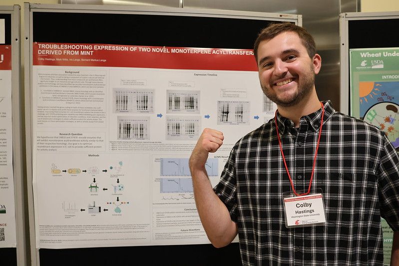 A person stands in front of an academic poster. He's pointing over his shoulder with his thumb at the poster.