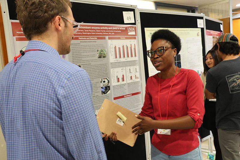 2 people talk in front of an academic poster.